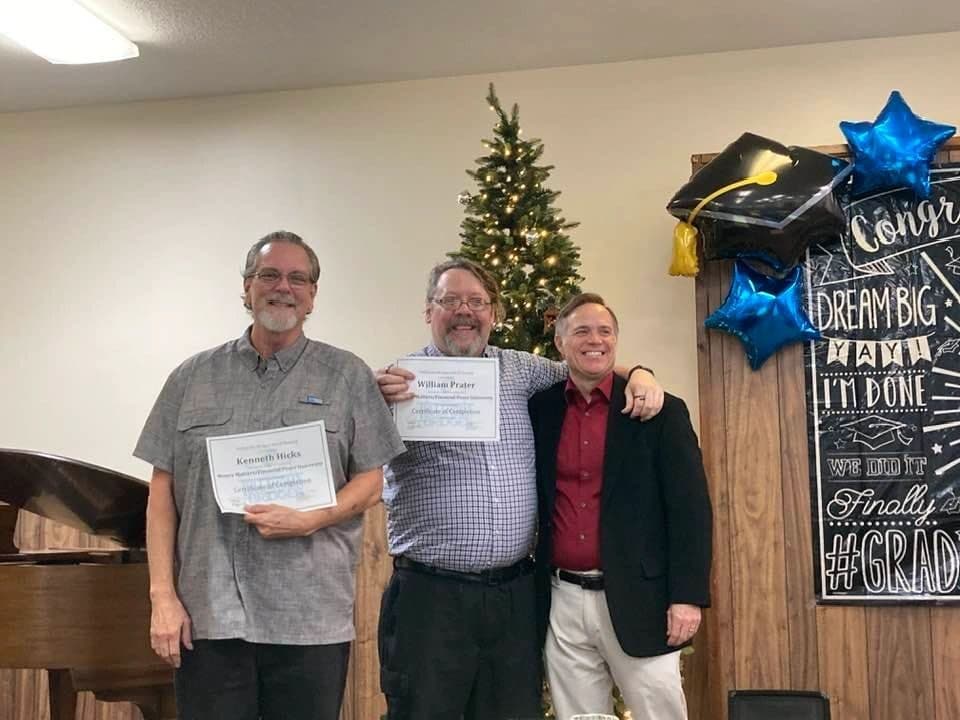 Two Getting Ahead graduates holding certificates with Ernie Jones in front of a Congrats Grad chalkboard.