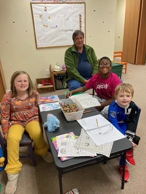 Four children coloring at a table with a volunteer during the Bridges for Students program.